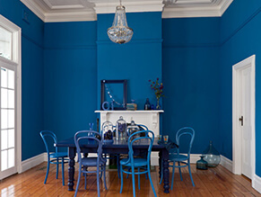 Bold blue feature dining room with white trims and doors and blue table and chairs and ornaments 